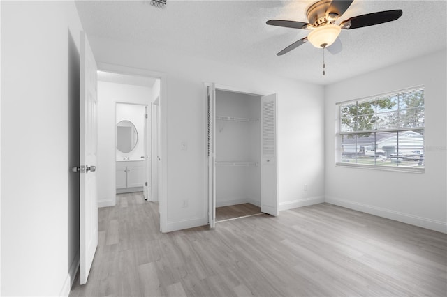 unfurnished bedroom with ceiling fan, light wood-type flooring, a textured ceiling, and a closet