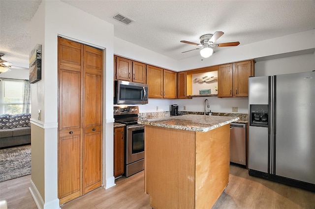 kitchen featuring a textured ceiling, stainless steel appliances, ceiling fan, light hardwood / wood-style floors, and a kitchen island