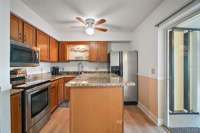 kitchen with light wood-type flooring, stainless steel appliances, sink, stone countertops, and a kitchen island