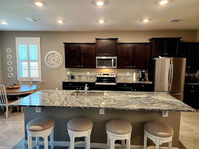 kitchen with sink, light tile patterned floors, stainless steel appliances, and a kitchen island with sink