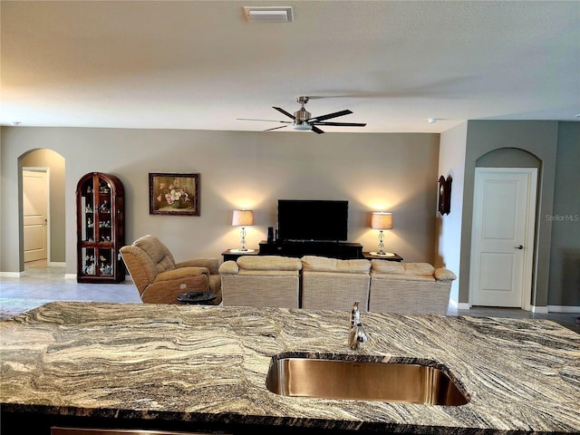 kitchen with light tile patterned flooring, stone countertops, ceiling fan, and sink