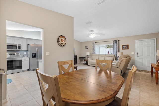 tiled dining room with ceiling fan, a textured ceiling, and vaulted ceiling