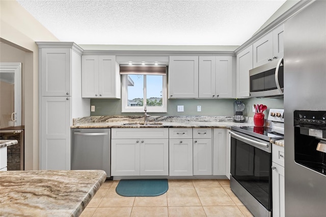 kitchen with sink, a textured ceiling, light tile patterned flooring, light stone counters, and stainless steel appliances