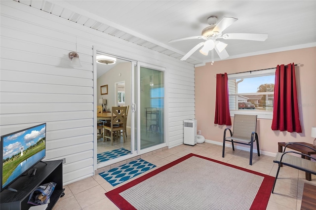 sitting room with ceiling fan, wooden walls, and light tile patterned flooring