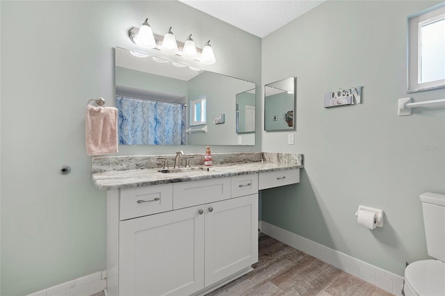 bathroom with a textured ceiling, vanity, toilet, and a wealth of natural light