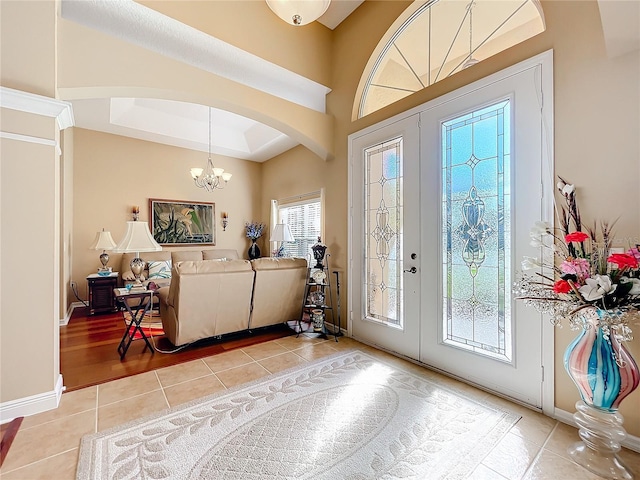 entrance foyer featuring a chandelier, light tile patterned floors, a tray ceiling, and french doors