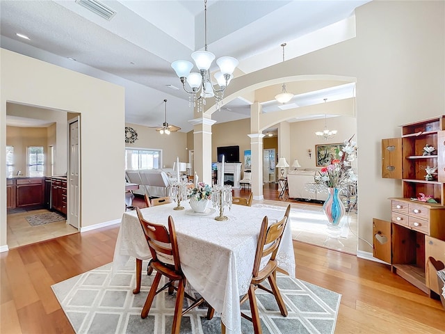 dining area featuring ceiling fan with notable chandelier, decorative columns, light hardwood / wood-style flooring, and lofted ceiling