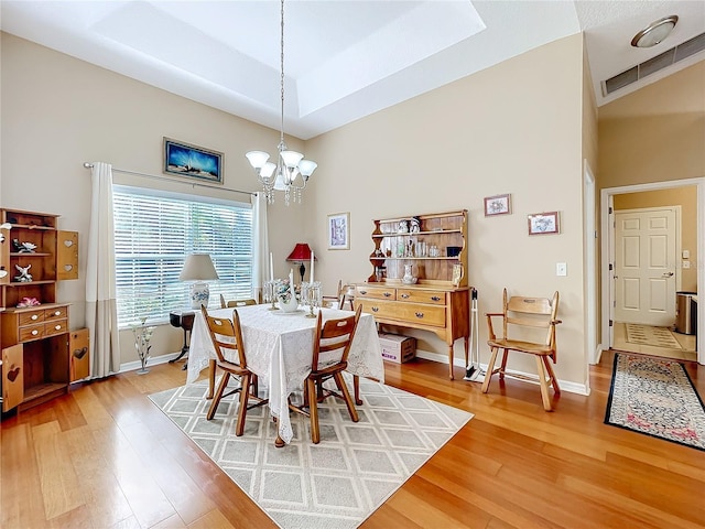 dining room with a raised ceiling, wood-type flooring, and an inviting chandelier