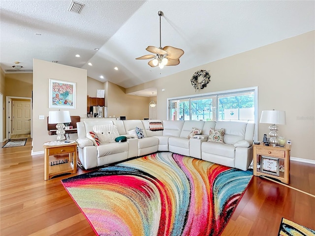 living room with a textured ceiling, ceiling fan, light hardwood / wood-style flooring, and vaulted ceiling