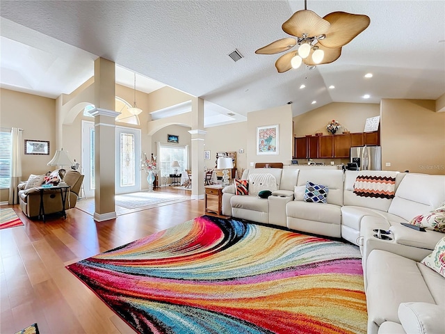 living room featuring hardwood / wood-style floors, lofted ceiling, ceiling fan, a textured ceiling, and decorative columns