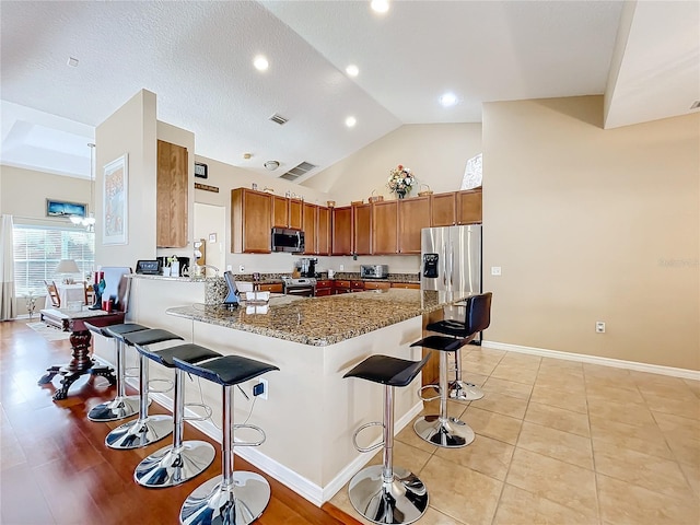 kitchen with high vaulted ceiling, kitchen peninsula, dark stone countertops, a breakfast bar, and appliances with stainless steel finishes