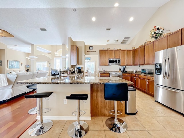 kitchen with stone counters, a breakfast bar, lofted ceiling, and appliances with stainless steel finishes