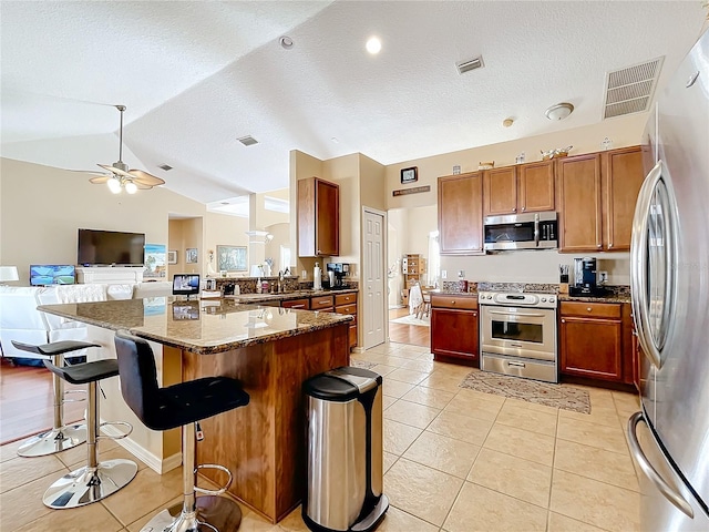 kitchen with a breakfast bar, lofted ceiling, dark stone countertops, light tile patterned floors, and stainless steel appliances