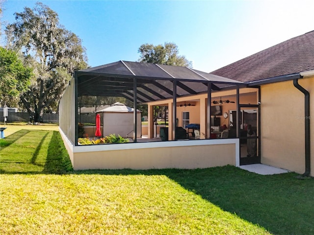 rear view of property with glass enclosure, ceiling fan, and a yard