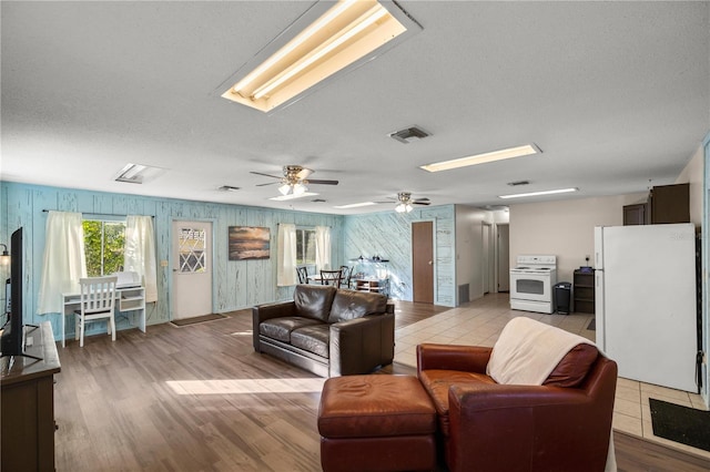 living room featuring a skylight, ceiling fan, a textured ceiling, and light wood-type flooring