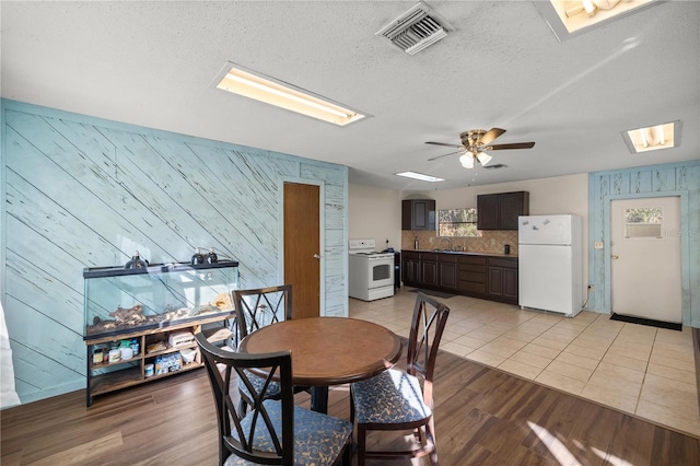 dining space featuring wood walls, sink, light hardwood / wood-style flooring, ceiling fan, and a textured ceiling