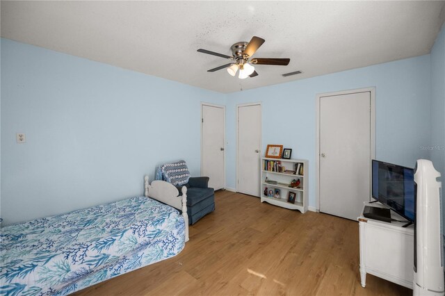 bedroom with wood-type flooring, a textured ceiling, two closets, and ceiling fan