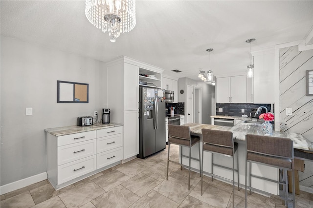 kitchen featuring pendant lighting, kitchen peninsula, white cabinetry, stainless steel appliances, and a chandelier