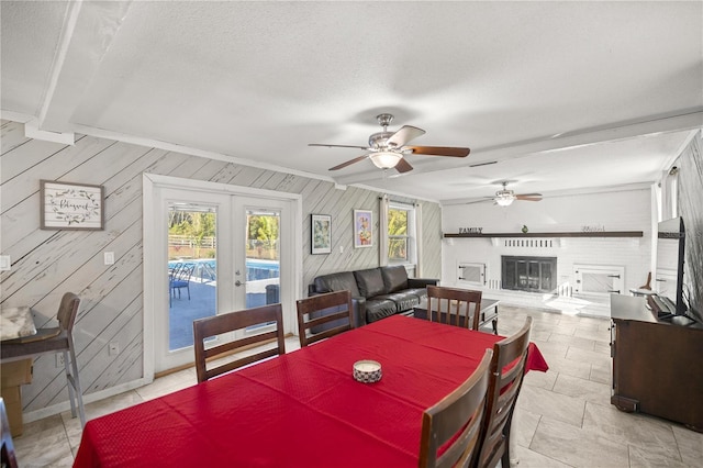 dining space with ceiling fan, french doors, a brick fireplace, a textured ceiling, and wooden walls