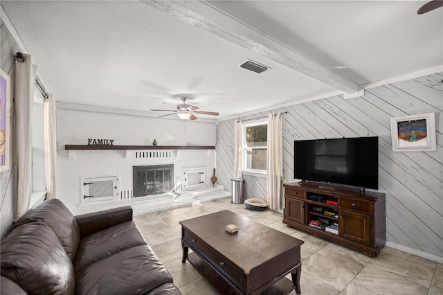 living room with beam ceiling, ceiling fan, a textured ceiling, wooden walls, and a fireplace