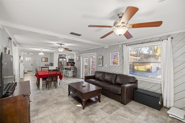 living room with beam ceiling, ceiling fan, french doors, and wooden walls