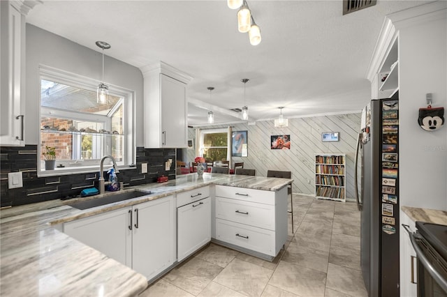 kitchen with kitchen peninsula, stainless steel fridge, sink, decorative light fixtures, and white cabinets