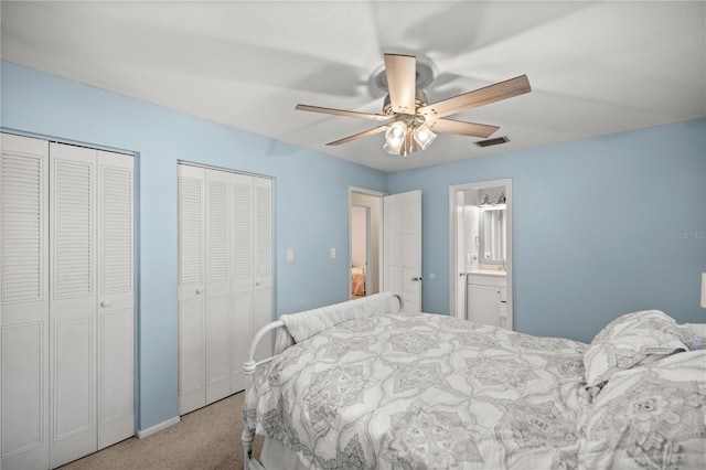 bedroom featuring ceiling fan, ensuite bath, light colored carpet, and multiple closets