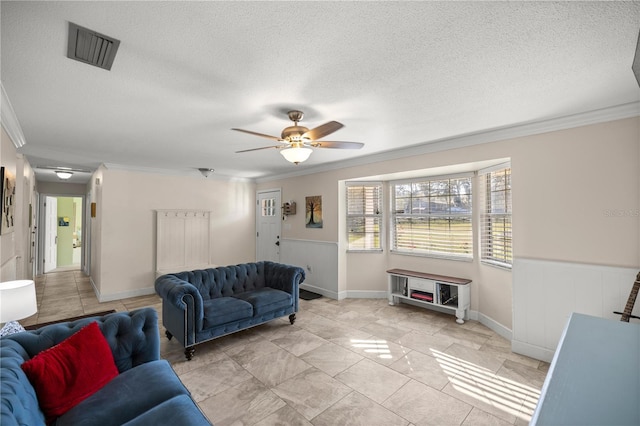 living room featuring a textured ceiling, ornamental molding, a wainscoted wall, and visible vents