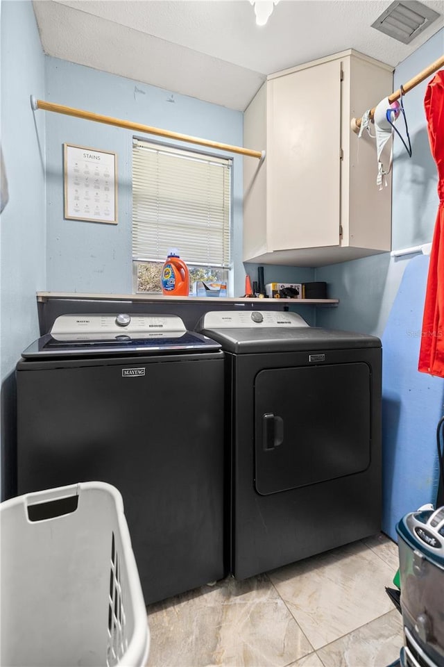 clothes washing area with washing machine and dryer, cabinet space, and visible vents