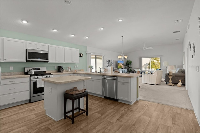 kitchen featuring a center island, appliances with stainless steel finishes, decorative light fixtures, a kitchen bar, and white cabinetry