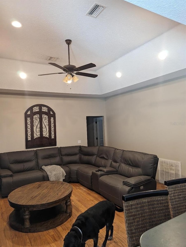 living room with ceiling fan, a raised ceiling, wood-type flooring, and a textured ceiling