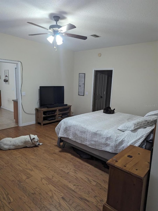 bedroom with a textured ceiling, hardwood / wood-style flooring, and ceiling fan