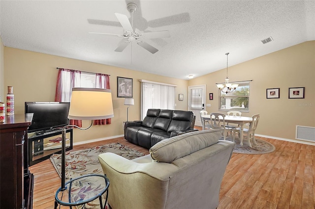 living room with lofted ceiling, a textured ceiling, light hardwood / wood-style flooring, and ceiling fan with notable chandelier