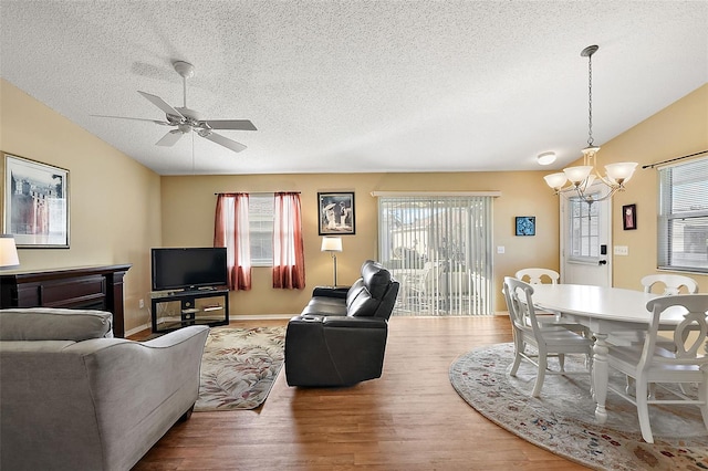 living room with ceiling fan with notable chandelier, wood-type flooring, and a textured ceiling