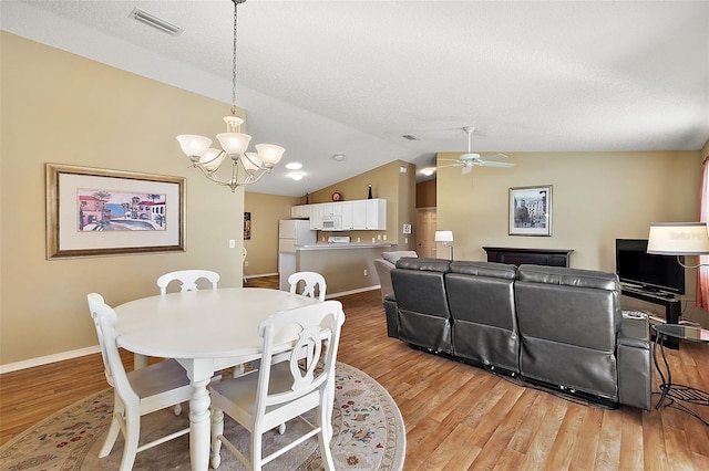 dining room with ceiling fan with notable chandelier, a textured ceiling, hardwood / wood-style floors, and vaulted ceiling