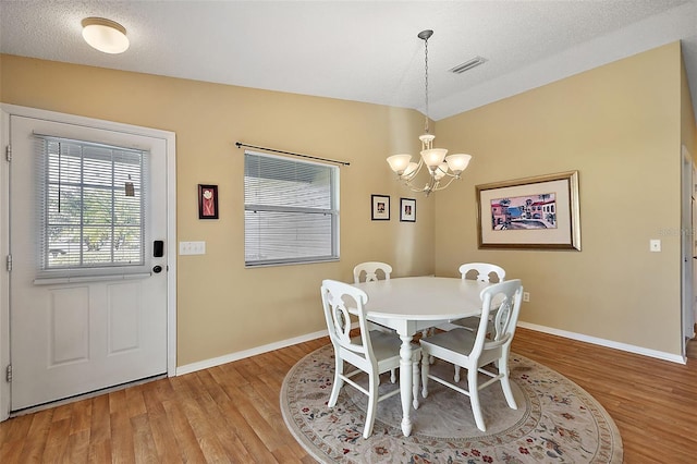 dining space featuring lofted ceiling, a textured ceiling, a chandelier, and hardwood / wood-style flooring