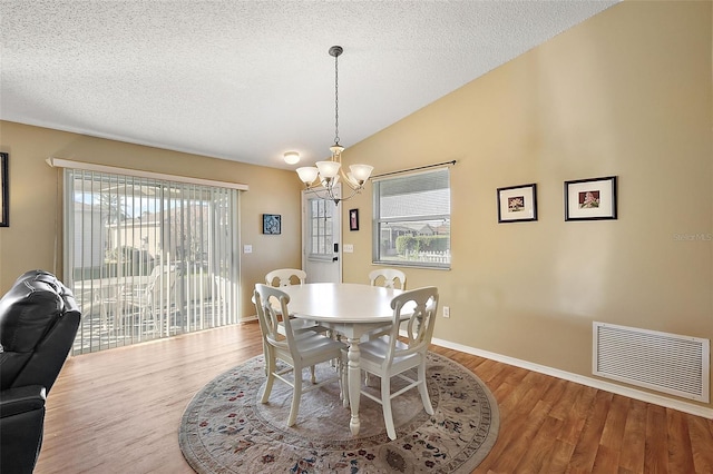 dining space featuring light hardwood / wood-style floors, vaulted ceiling, a textured ceiling, and a chandelier