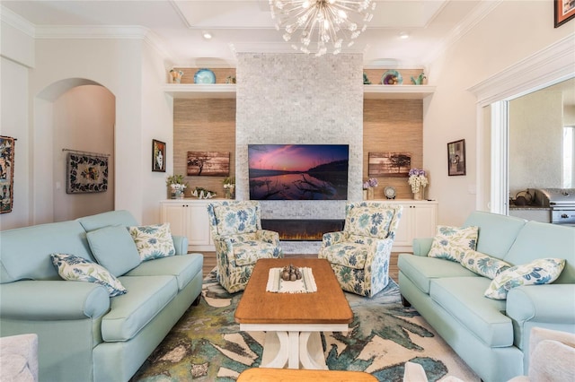 living room with built in features, ornamental molding, a fireplace, and a chandelier