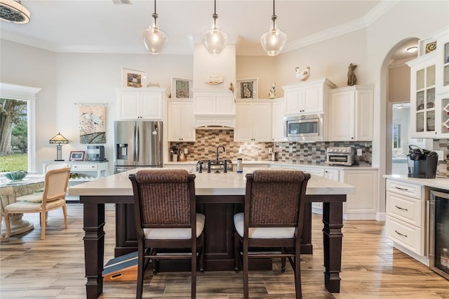 kitchen with a center island with sink, white cabinets, decorative light fixtures, and appliances with stainless steel finishes