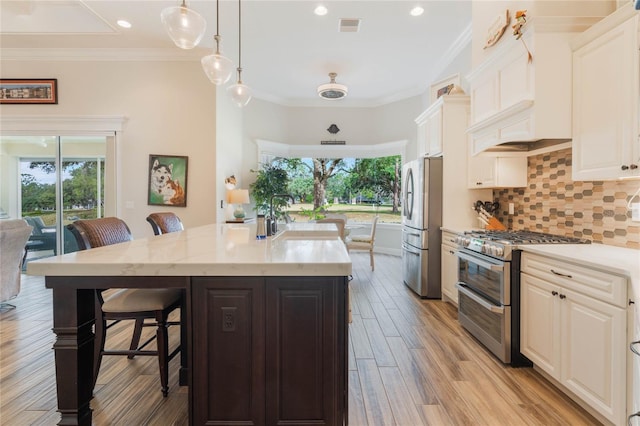 kitchen with a breakfast bar, a kitchen island with sink, white cabinets, hanging light fixtures, and stainless steel appliances