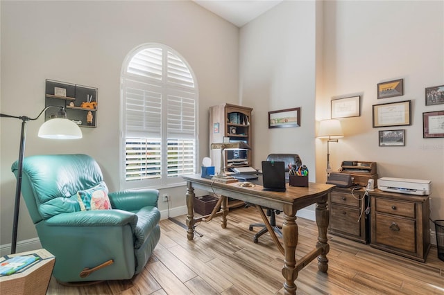 home office with light hardwood / wood-style flooring and a high ceiling