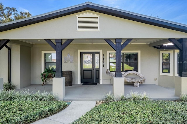 view of exterior entry with covered porch and stucco siding