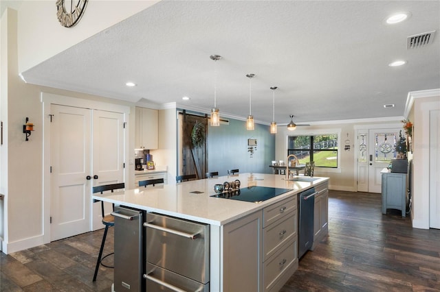 kitchen featuring a barn door, visible vents, dark wood-type flooring, a kitchen island with sink, and black electric stovetop