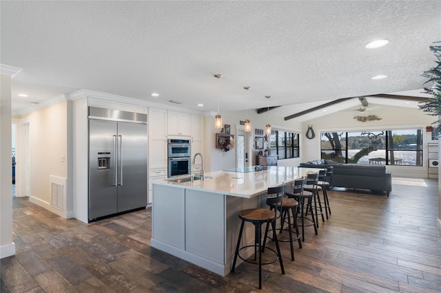 kitchen featuring vaulted ceiling with beams, stainless steel appliances, dark wood-type flooring, and white cabinetry