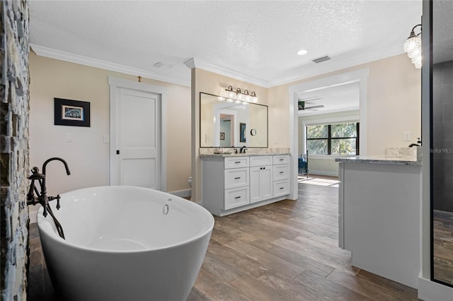 full bathroom with ornamental molding, vanity, a textured ceiling, wood finished floors, and a freestanding tub