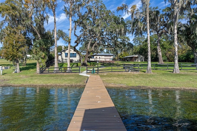 view of dock featuring a lawn, a water view, and fence