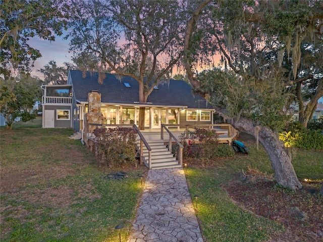 back house at dusk featuring a lawn and a deck