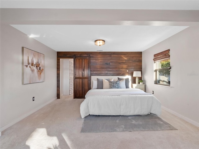 bedroom featuring light carpet, wooden walls, and a barn door