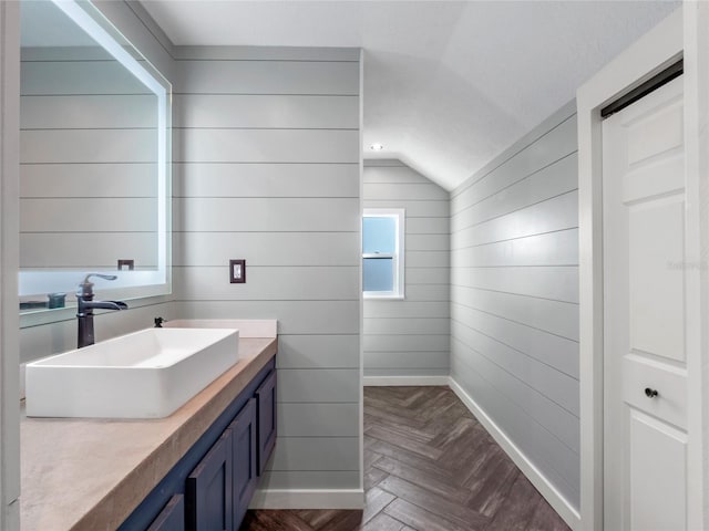 bathroom with lofted ceiling, wooden walls, vanity, and parquet flooring