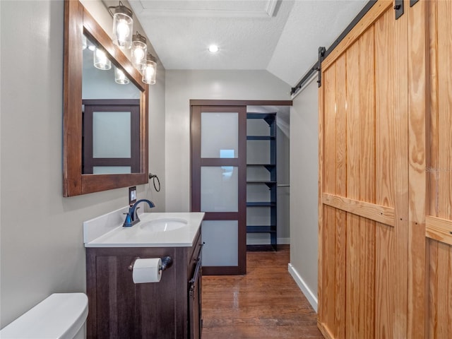 bathroom with a textured ceiling, vaulted ceiling, hardwood / wood-style floors, toilet, and vanity